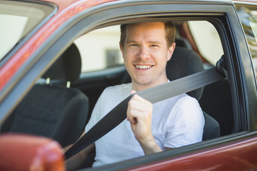 Junger Mann sitzt im Auto und schnallt sich an